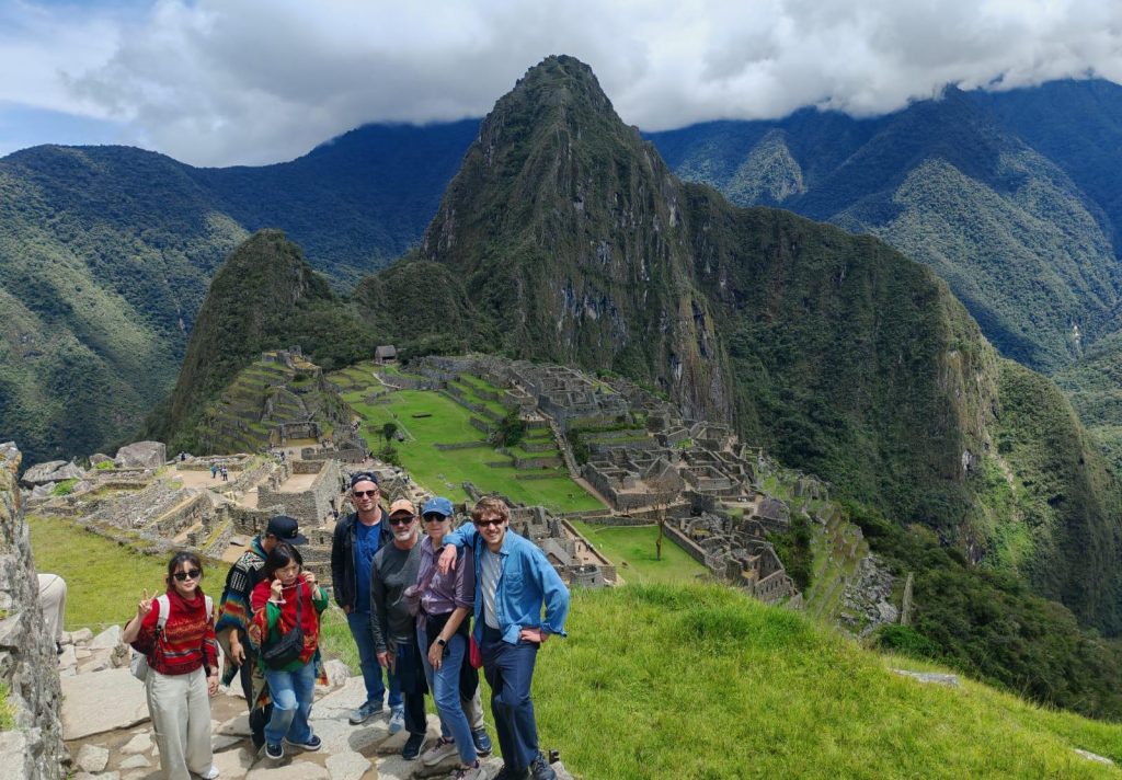 Group of tourists posing at Machu Picchu with the classic citadel view and Huayna Picchu mountain