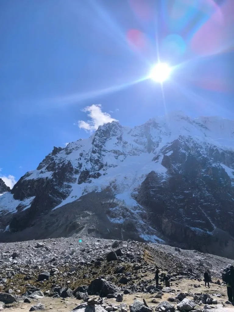 Trekkers walking below the snow-covered Salkantay massif beneath intense high-altitude sunlight.