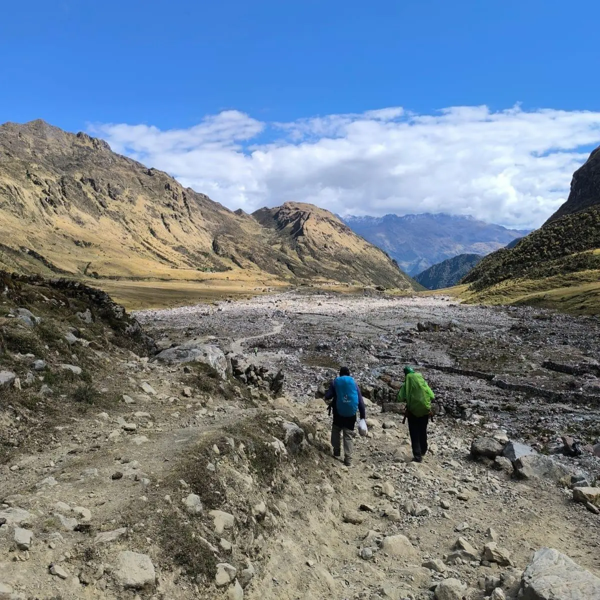 Two hikers descending a rocky trail through the high-Andean landscape of the Salkantay Trek.