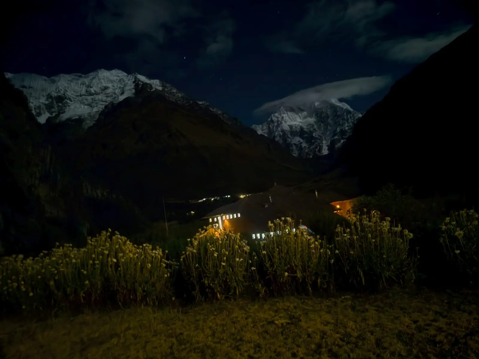 Snow-covered mountains and illuminated camp buildings beneath the night sky on the Salkantay route.