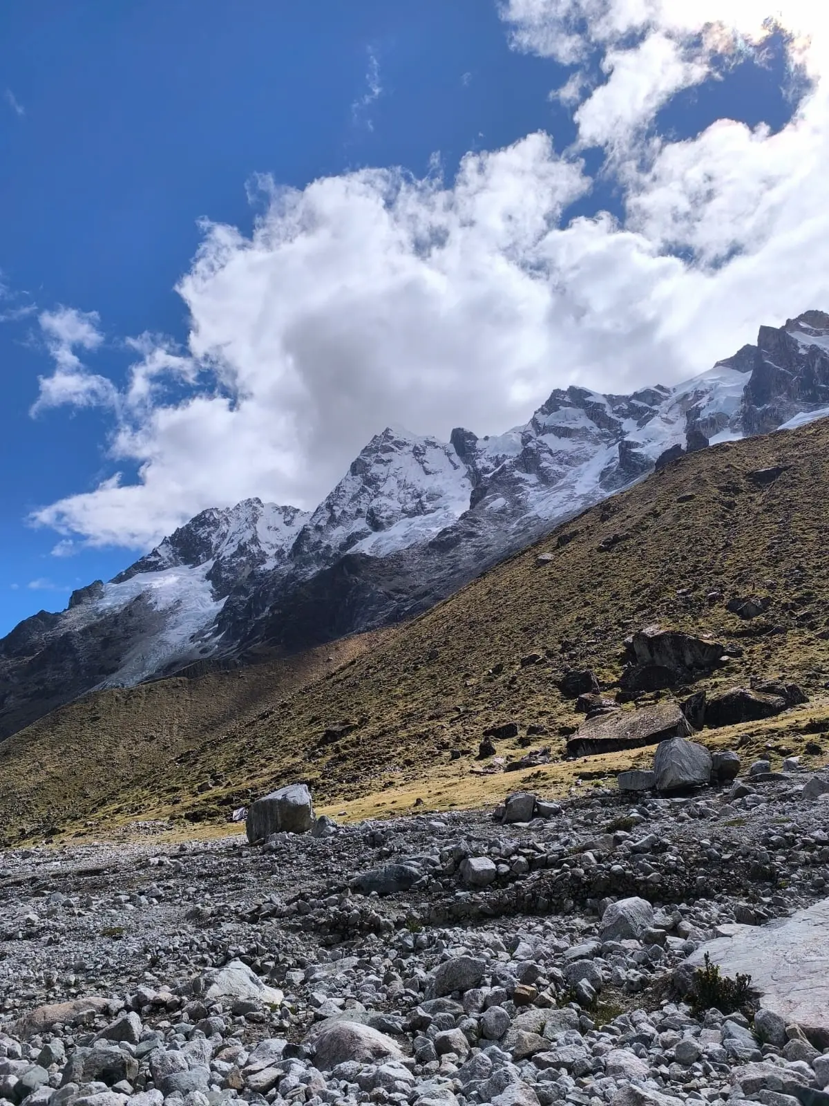 Snow-covered Andean peaks rising above a rocky landscape beneath large white clouds on the Salkantay route.