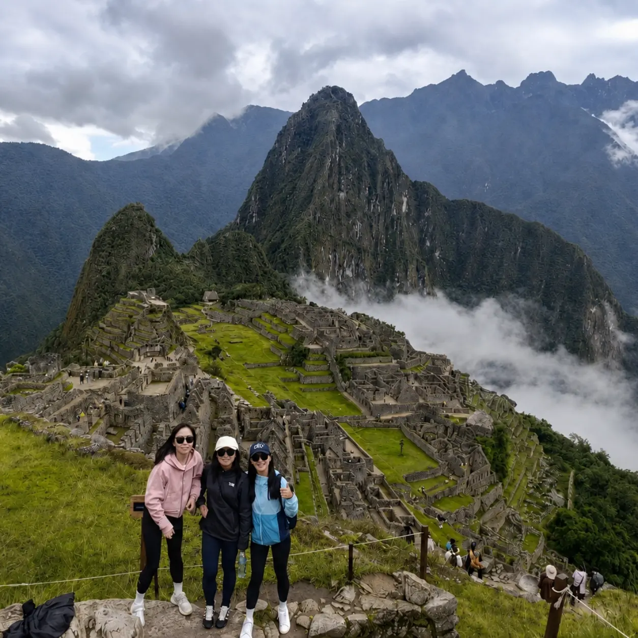 Three travelers posing above the Machu Picchu citadel as clouds and mist drift