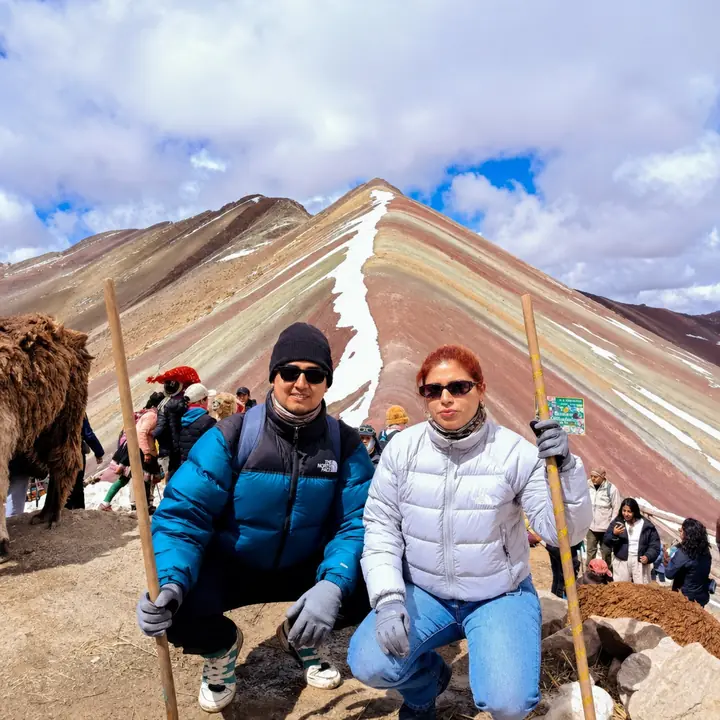 Two hikers kneeling with walking sticks before Rainbow Mountain.