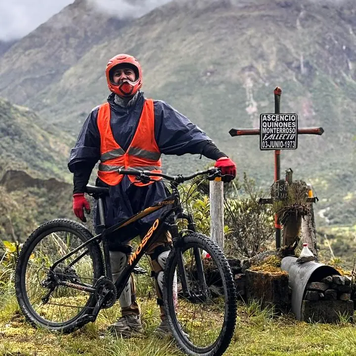 Mountain biker standing beside a roadside memorial on the Inca Jungle route.