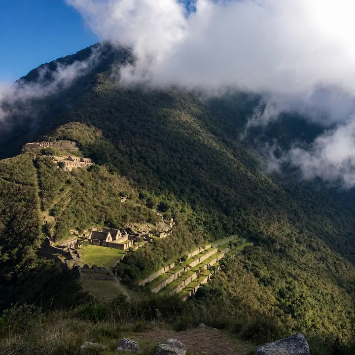 Choquequirao ruins appearing through clouds on a forested ridge.