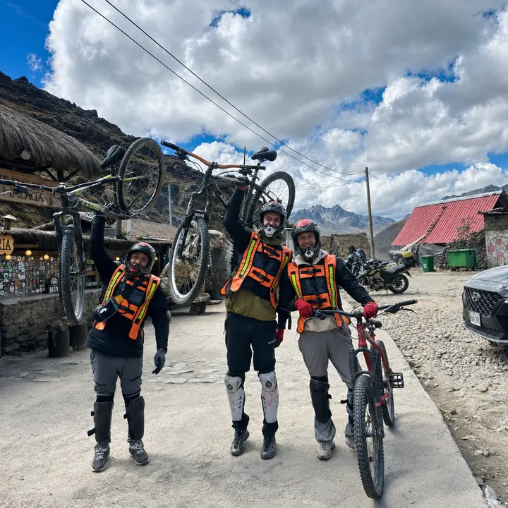Three cyclists celebrating with mountain bikes at a high Andean pass.