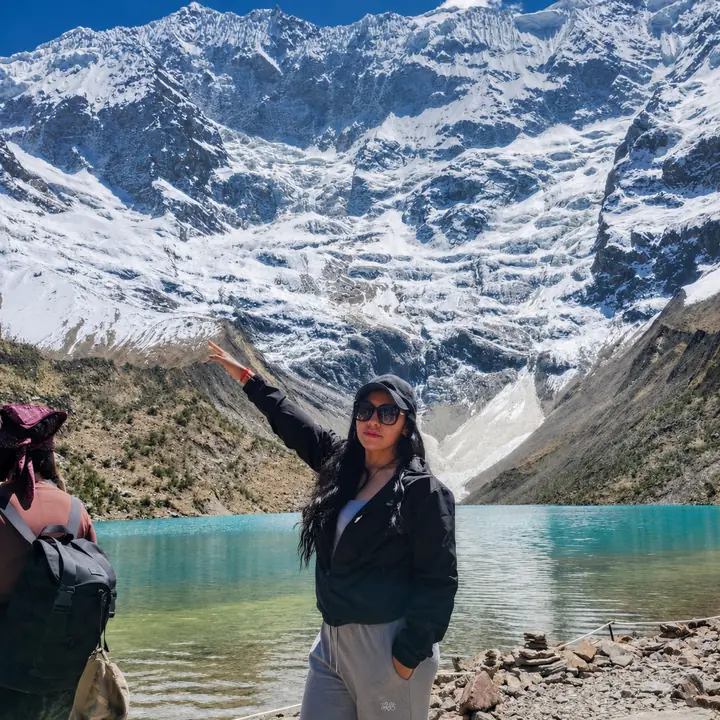 Woman pointing toward the glacier above turquoise Humantay Lake.