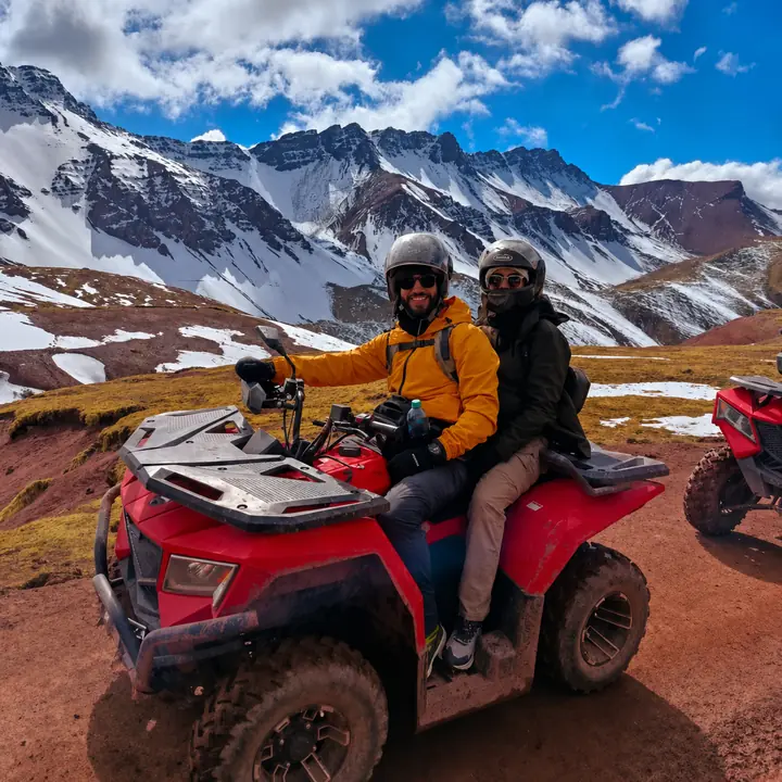 Couple riding a red ATV through a high-altitude snowy mountain landscape.