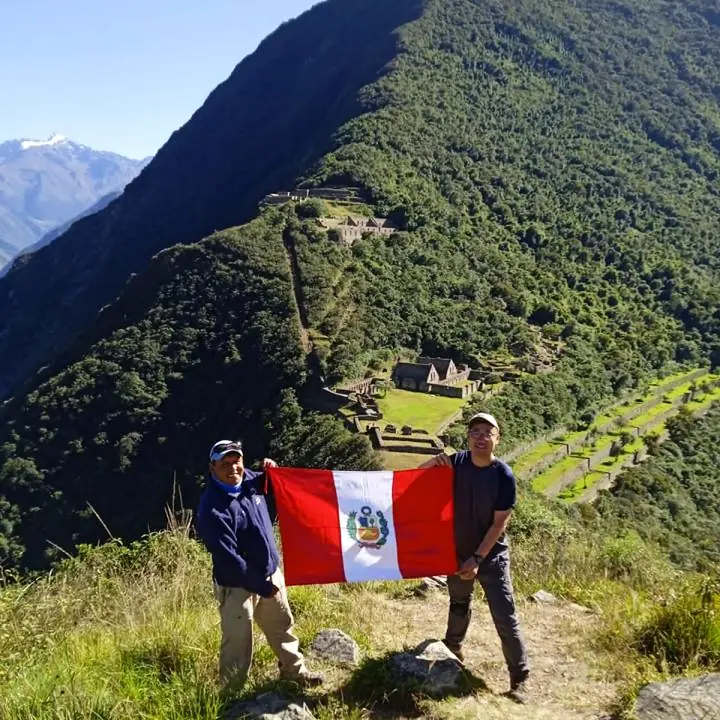 Travelers holding Peru's flag at a Choquequirao viewpoint.