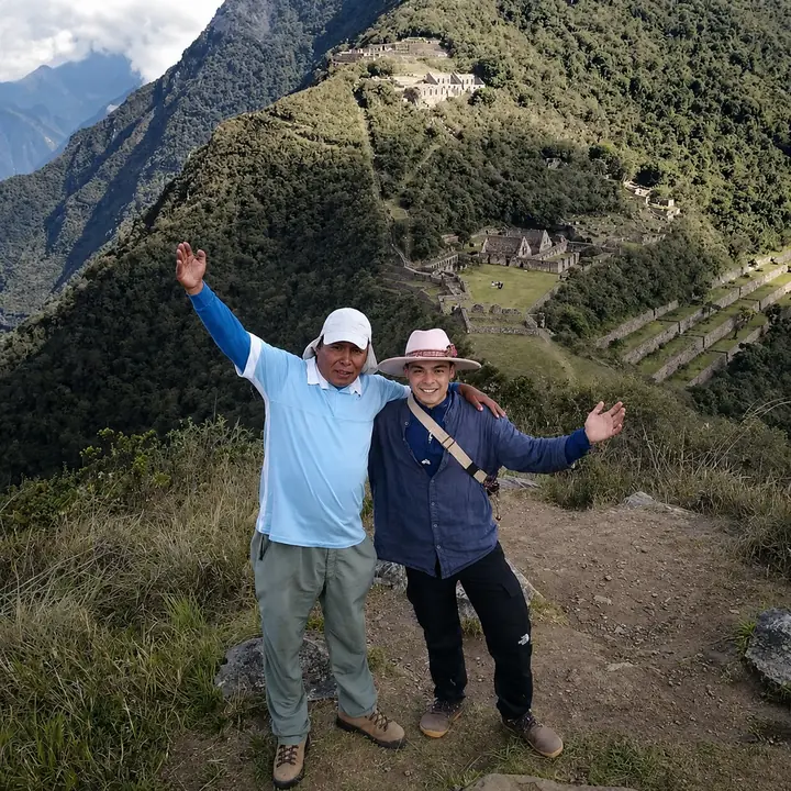 Two travelers celebrating with Choquequirao visible across the valley.