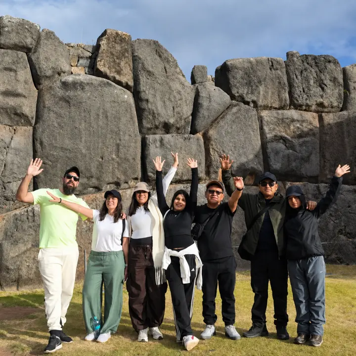 Travel group raising their hands before the ancient walls of Sacsayhuaman.