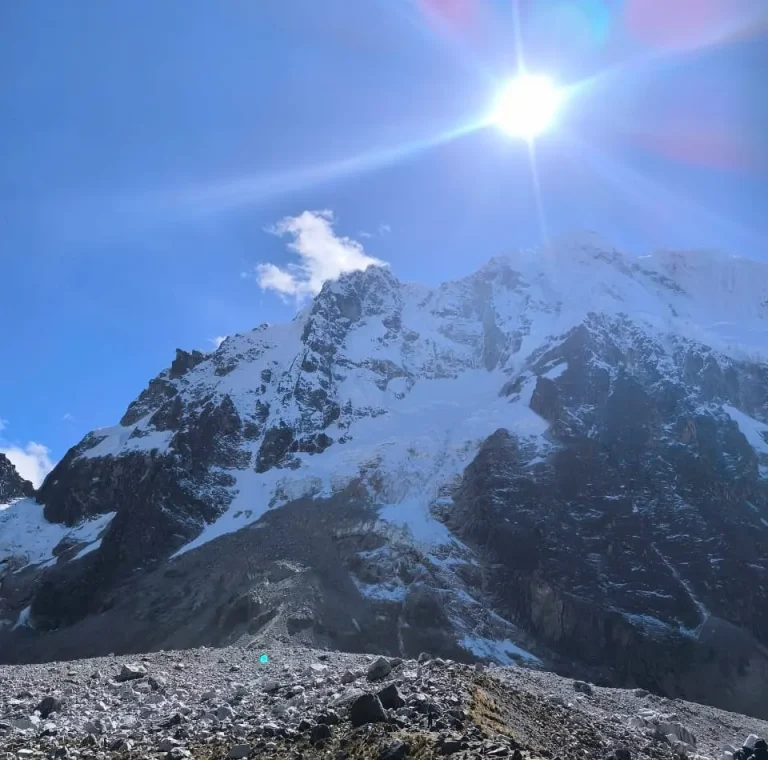 Trekkers walking below the snow-covered Salkantay massif beneath intense high-altitude sunlight.