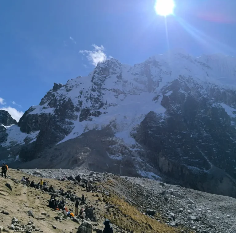 Hikers resting below the snow-covered Salkantay massif under bright high-altitude sunlight.