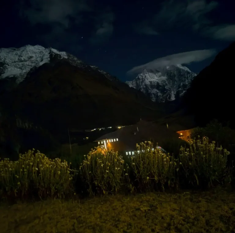 Snow-covered mountains and illuminated camp buildings beneath the night sky on the Salkantay route.