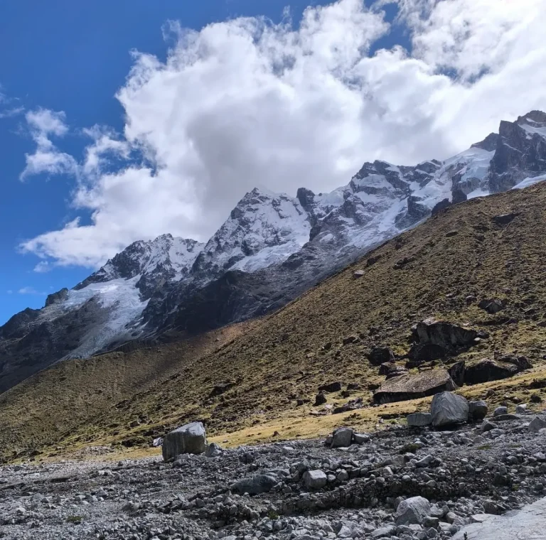 Snow-covered Andean peaks rising above a rocky landscape beneath large white clouds on the Salkantay route.