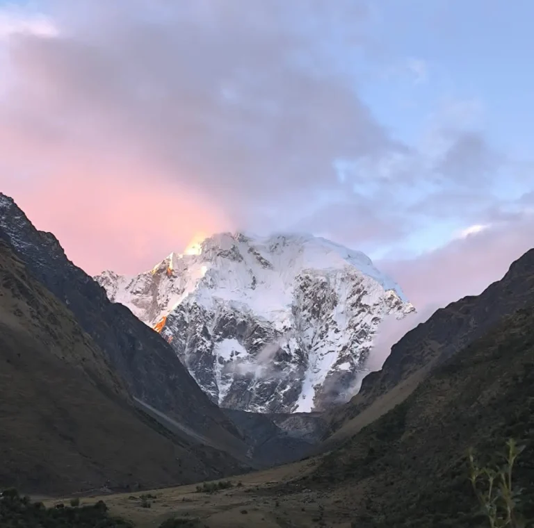 Pink sunrise illuminating the snowy Salkantay Mountain between steep Andean valley walls.