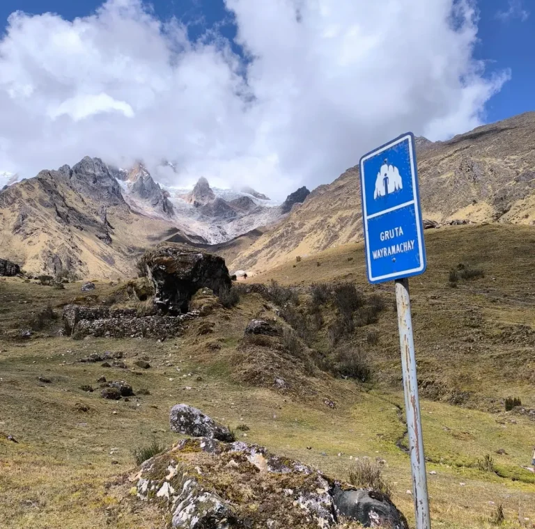 Wayramachay Cave sign with high Andean mountains in the background along the Salkantay route.